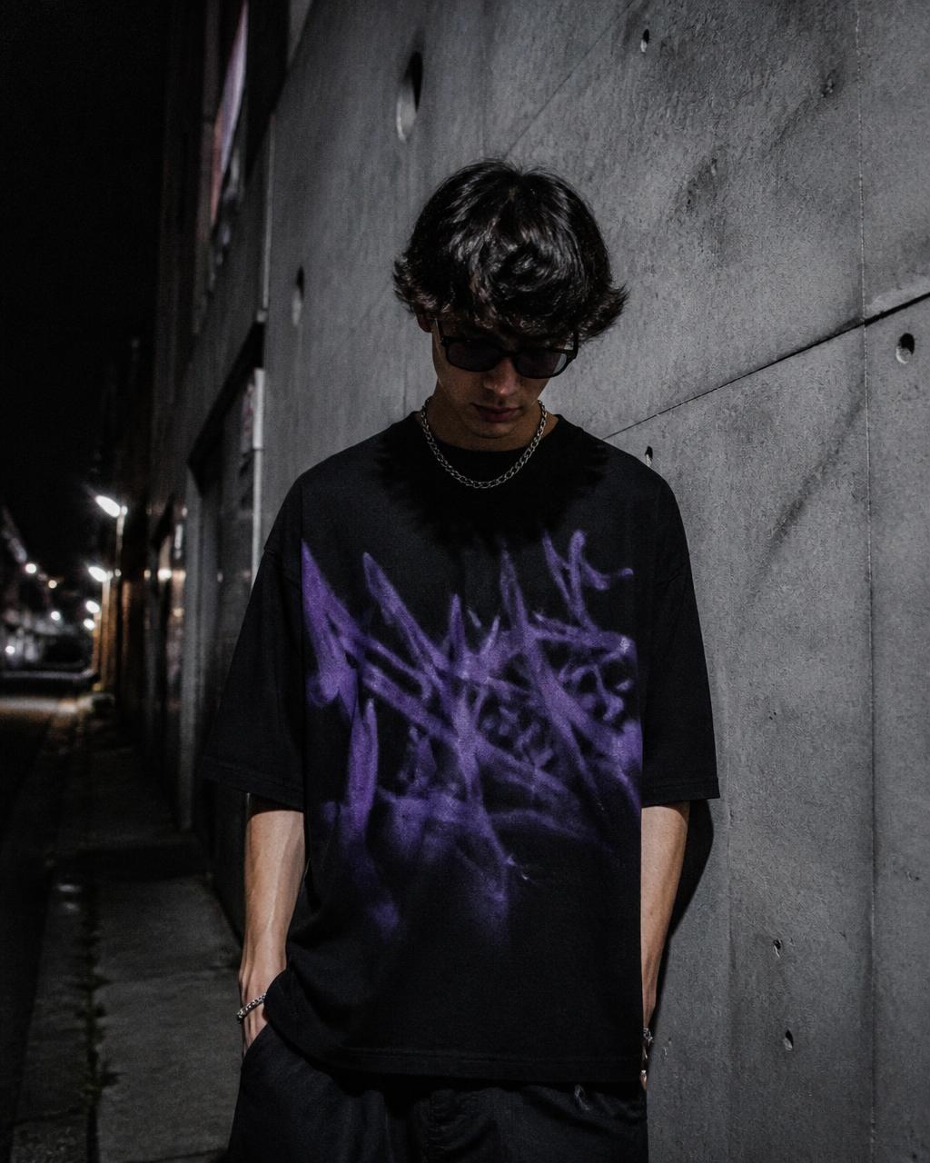 Persona vistiendo la camiseta oversize aerografiada en un callejón de concreto de noche